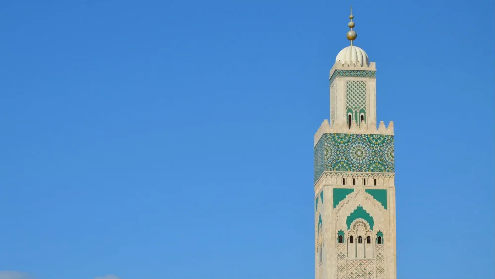 Le minaret de la mosquée Hassan II à Casablanca, orné de zellige vert, se détache sur un ciel bleu.
